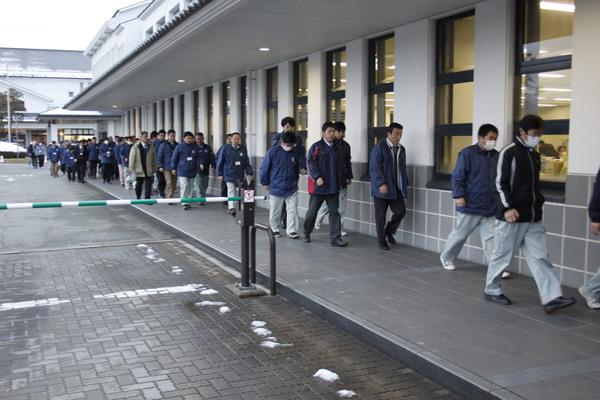 職員たちが建物の横を縦に並んで歩いている写真